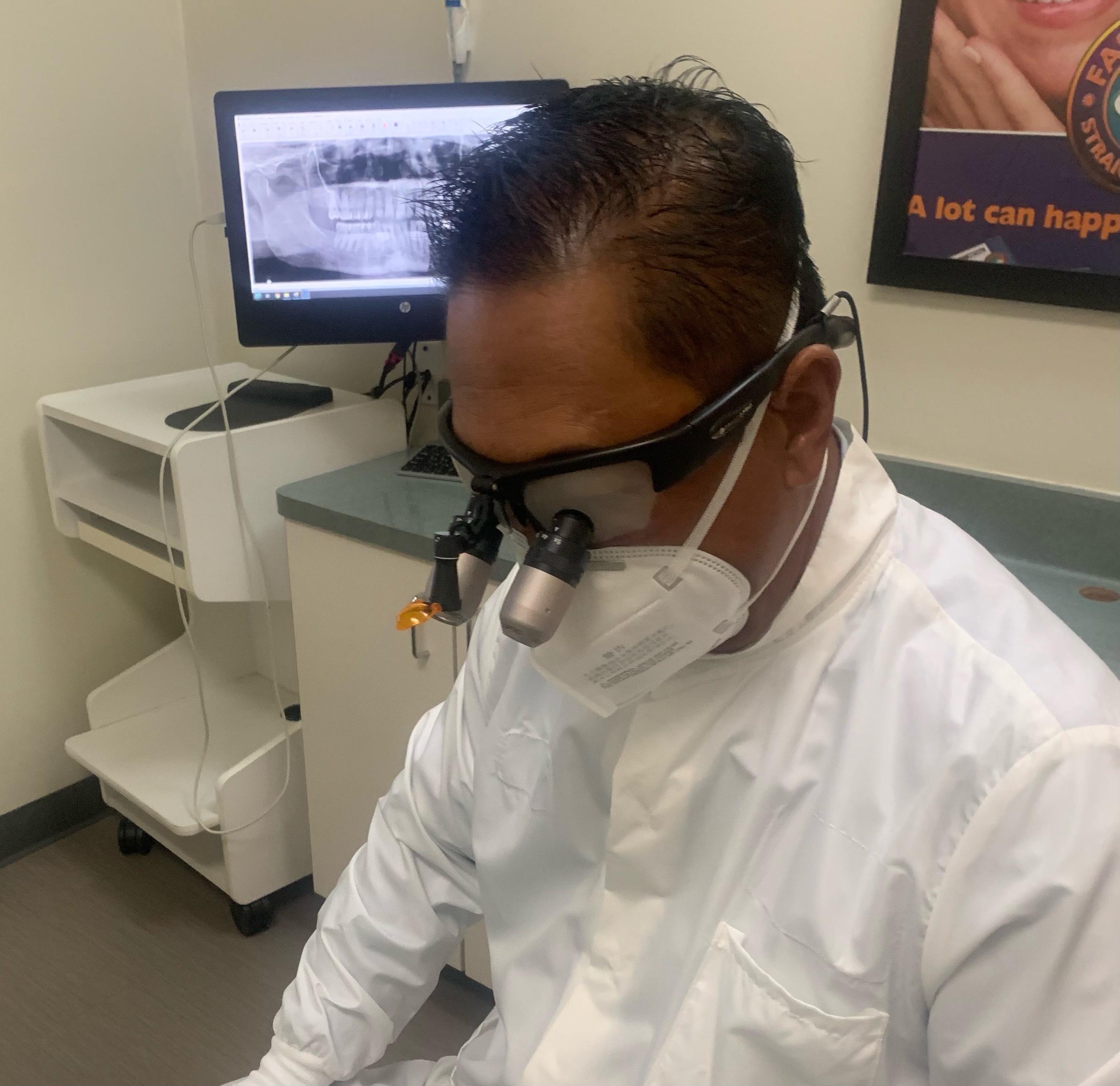 Dr. Ron E. Quibilan at work in loupes and a mask, with a digital x-ray on the monitor beside him.
