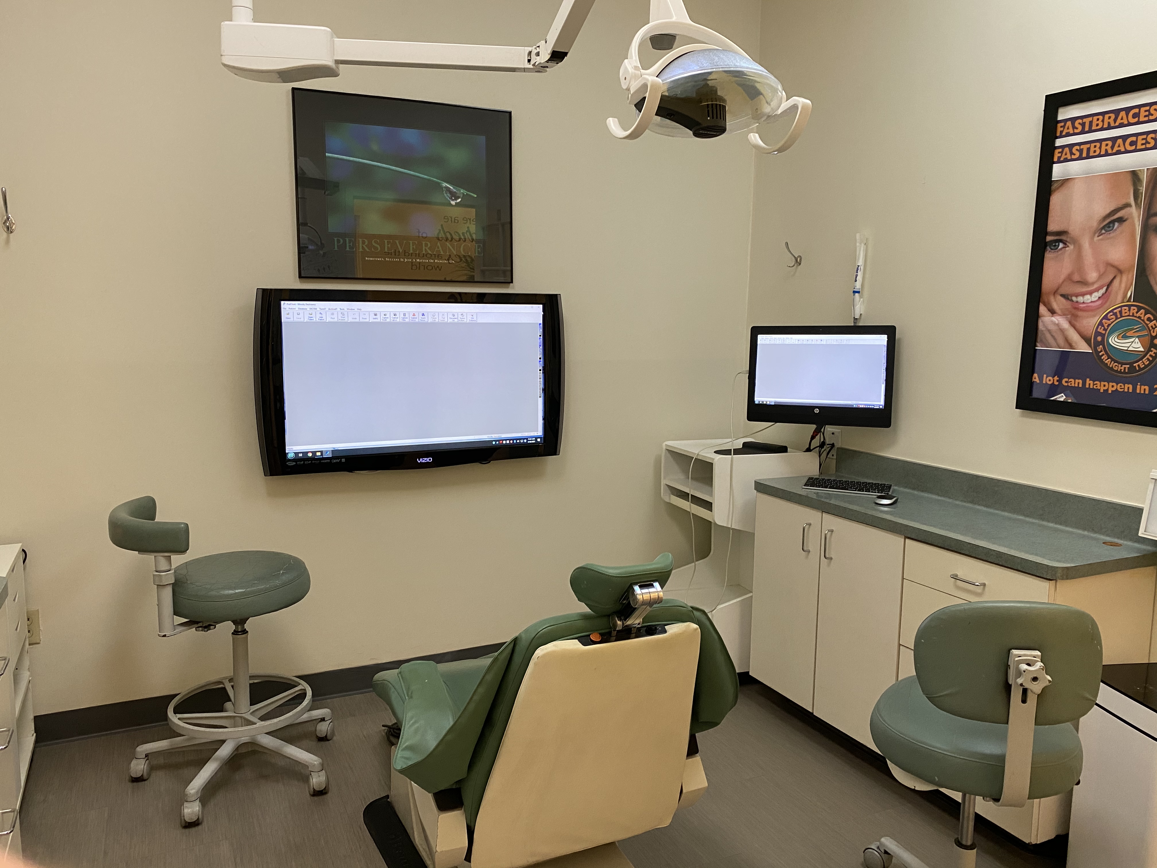 Quibilan Dentistry treatment room with sage-green chairs, digital monitors, and a Fastbraces poster on the wall.